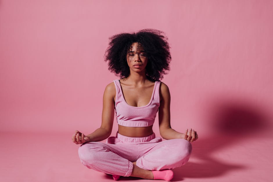 A woman with afro hair meditates in a peaceful studio with pink surroundings, embodying relaxation and zen