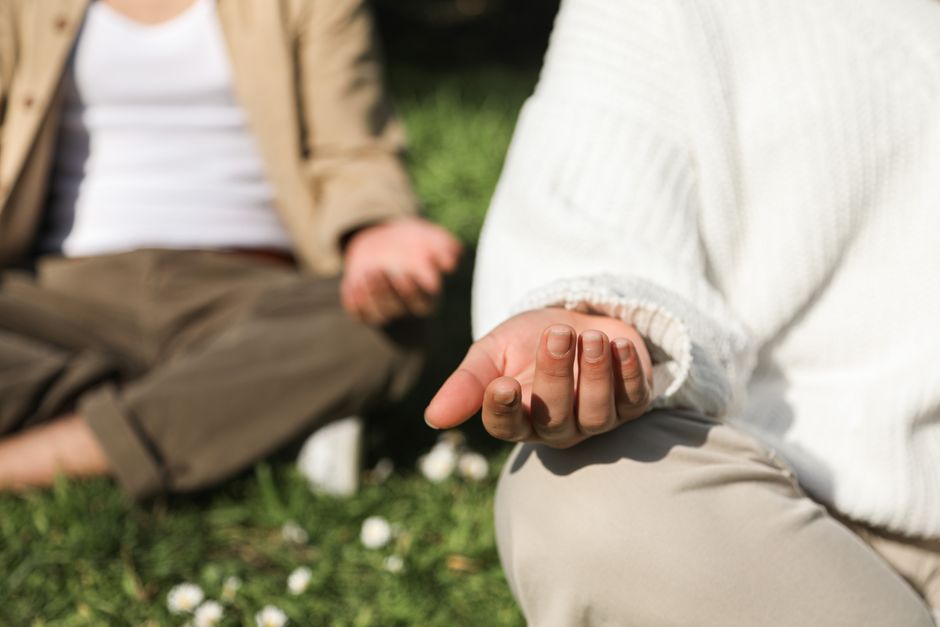 Two people meditating outdoors, focusing on hands in a peaceful setting