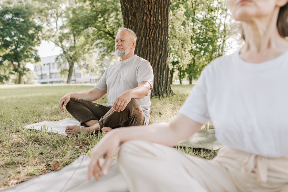 Elderly man and woman meditating outdoors on yoga mats in a peaceful park setting